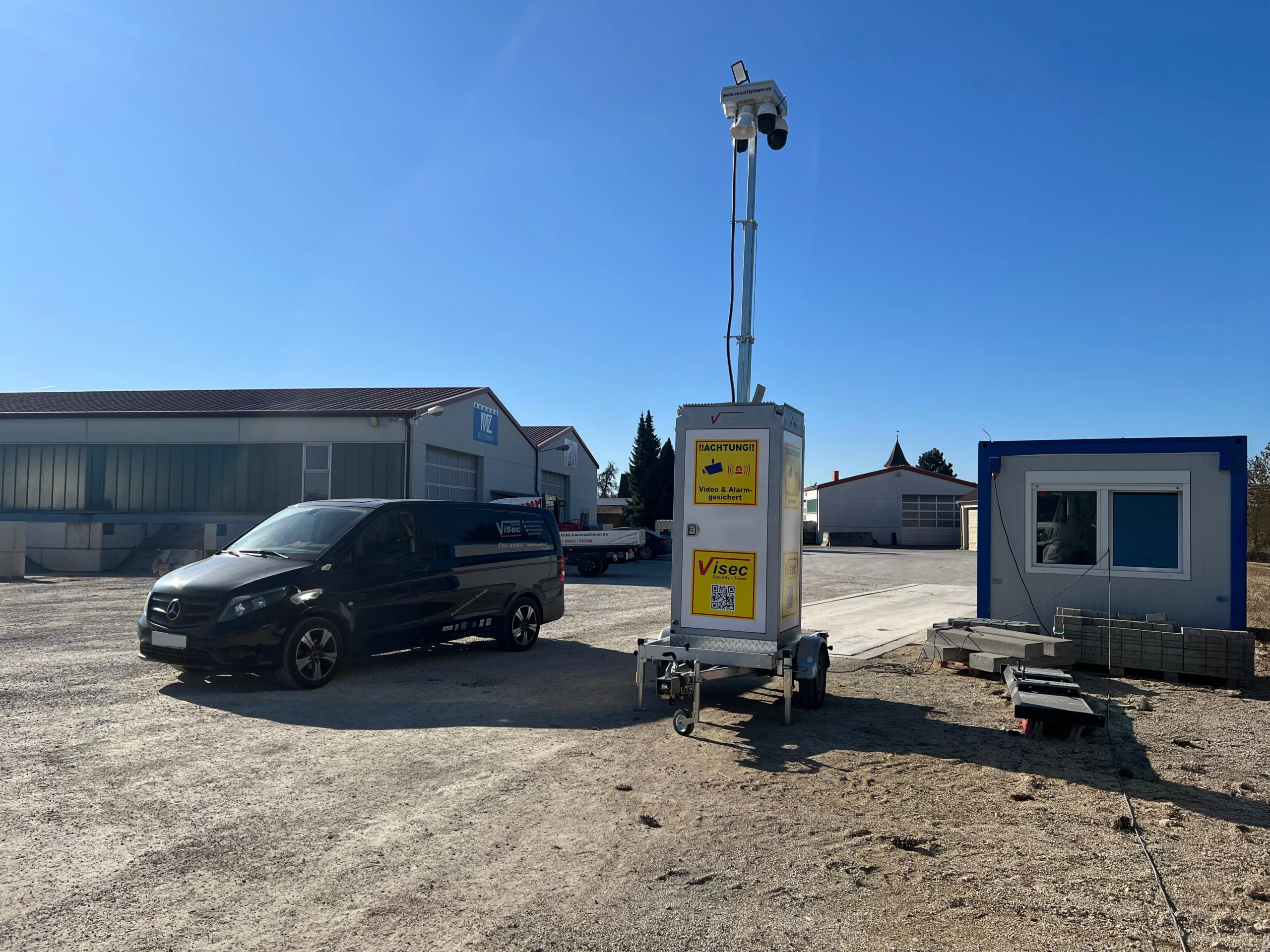 Mobiler Videoturm der ViSec GmbH zur Baustellenüberwachung, neben einem schwarzen Mercedes-Transporter und einem blauen Container, bei sonnigem Wetter auf einem Firmengelände.