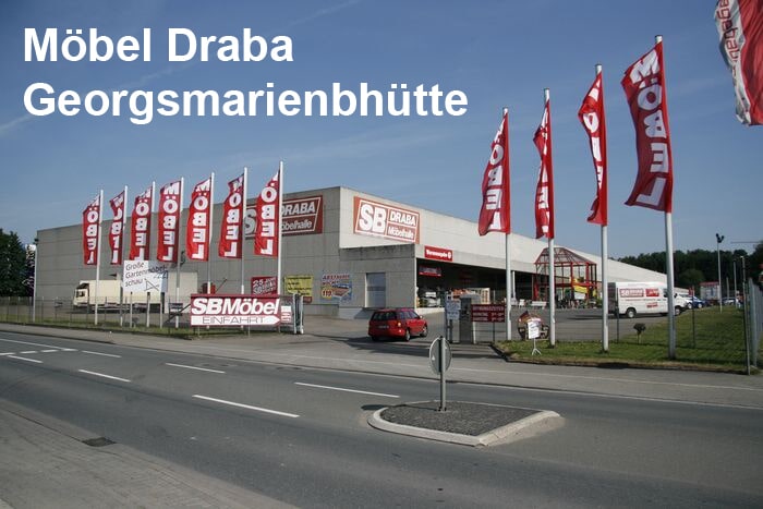 Ein Möbelgeschäft namens "Möbel Draba" mit roten Fahnen und einem Parkplatz an einem klaren Tag.