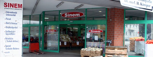 Eingang eines internationalen Lebensmittelgeschäfts namens "Sinem" mit Obstkisten und Werbeschild.