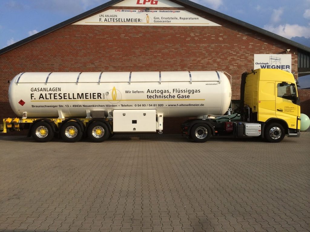 Ein gelber Tanklastwagen von "F. Altesellmeier" ist vor einem Backsteingebäude geparkt.