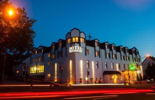 Ein modernes, mehrstöckiges Hotel mit warm beleuchteter Fassade und vorbeifahrenden Autos bei Nacht.