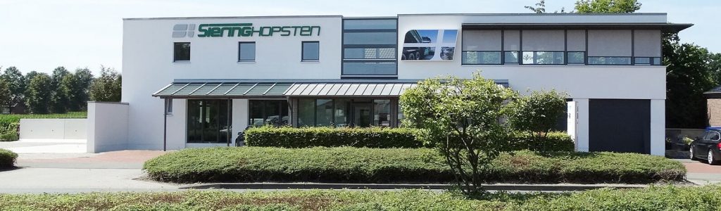 Modernes weißes Bürogebäude mit klaren Linien, umgeben von gepflegter Hecke und Baum.