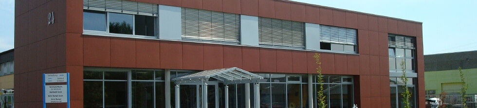 Modernes zweistöckiges Gebäude mit roter Fassade, großen Fenstern und gläsernem Eingangsbereich.