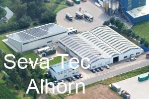 Luftaufnahme eines Industriegebiets mit Lagerhallen, Solarpaneelen und parkenden Fahrzeugen.