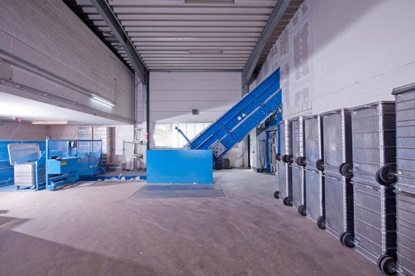 Industrielle Halle mit blauem Förderband, metallenen Containern und einer blauen Maschine.