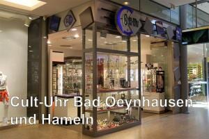 Eingang eines modernen Uhrengeschäfts mit Glasfront und hell beleuchtetem Innenraum in einem Einkaufszentrum.